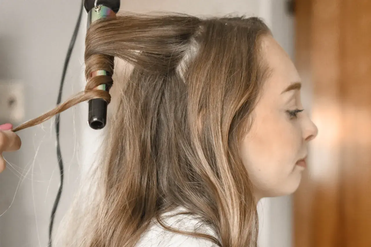 Creando peinados fáciles y rápidos: una mano riza el cabello de una mujer con una plancha.
