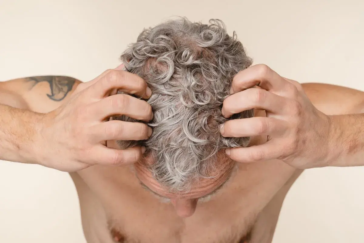 Hombre rascándose el cuero cabelludo con pelo gris y rizado.