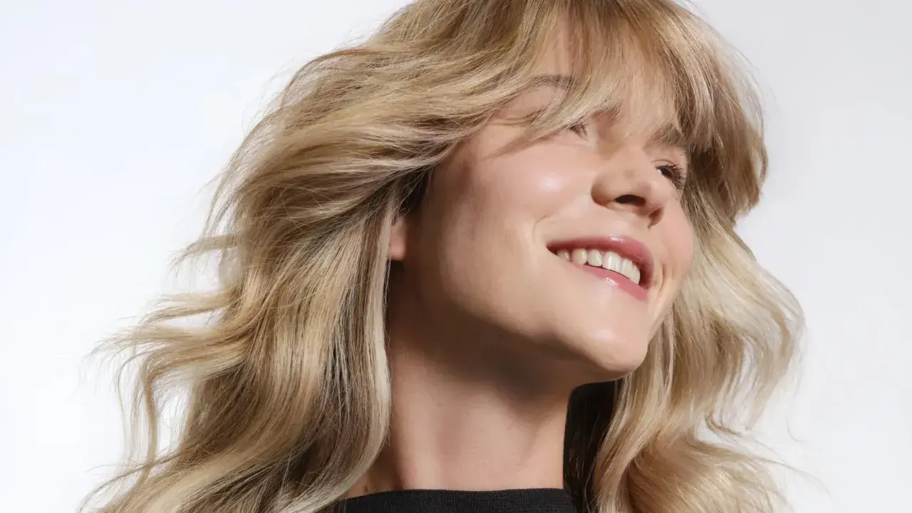 Mujer sonriendo con cabello rubio claro ondulado y brillante.