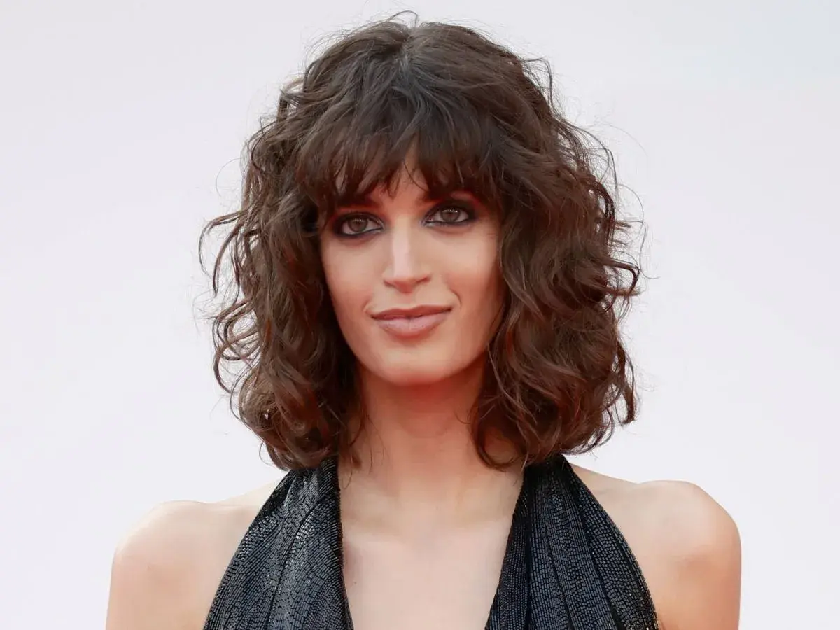 Mujer con curly pelo corto rizado natural, mirada intensa y vestido negro brillante.