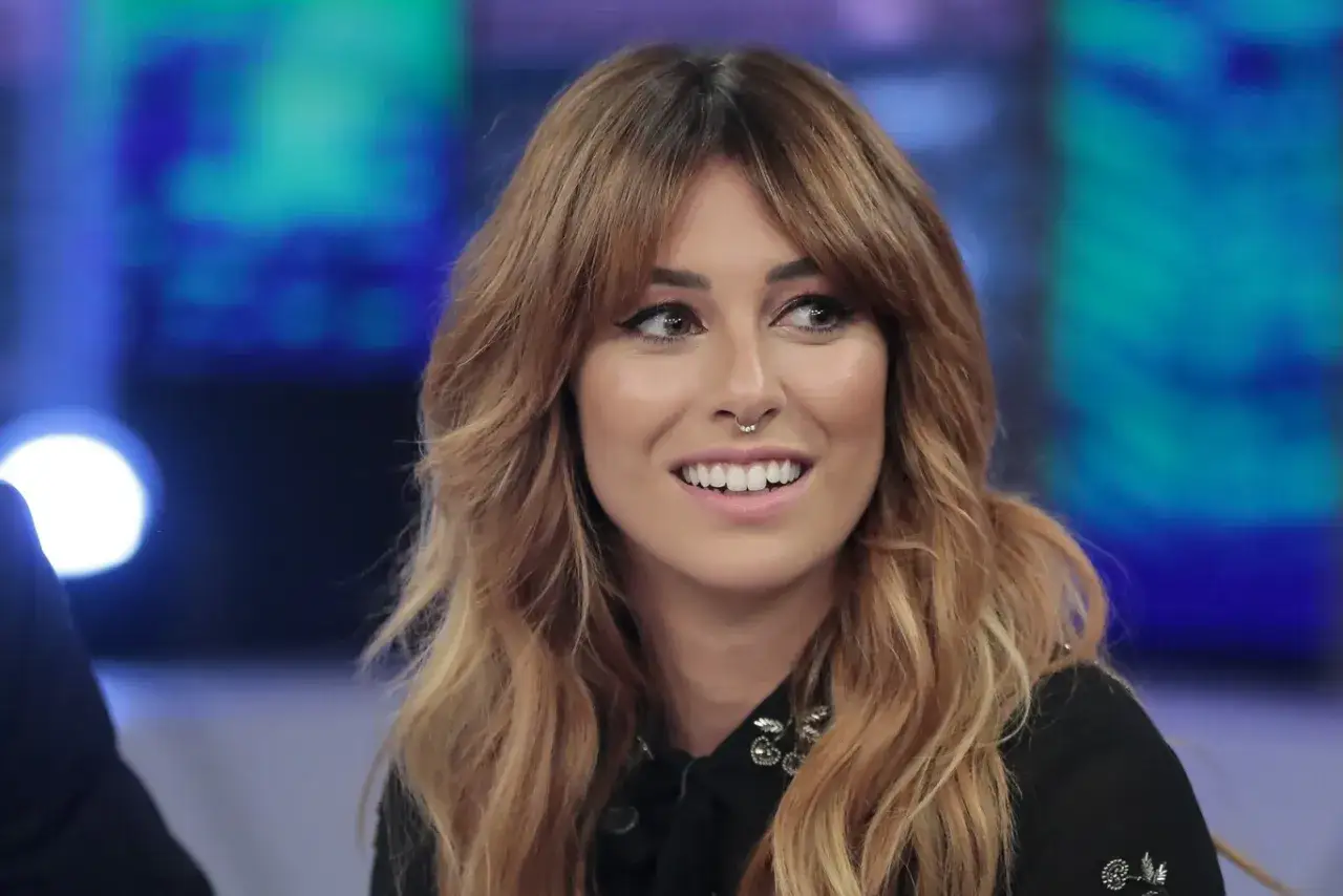 Mujer sonríe con su cabello castaño ondulado y flequillo cortina.