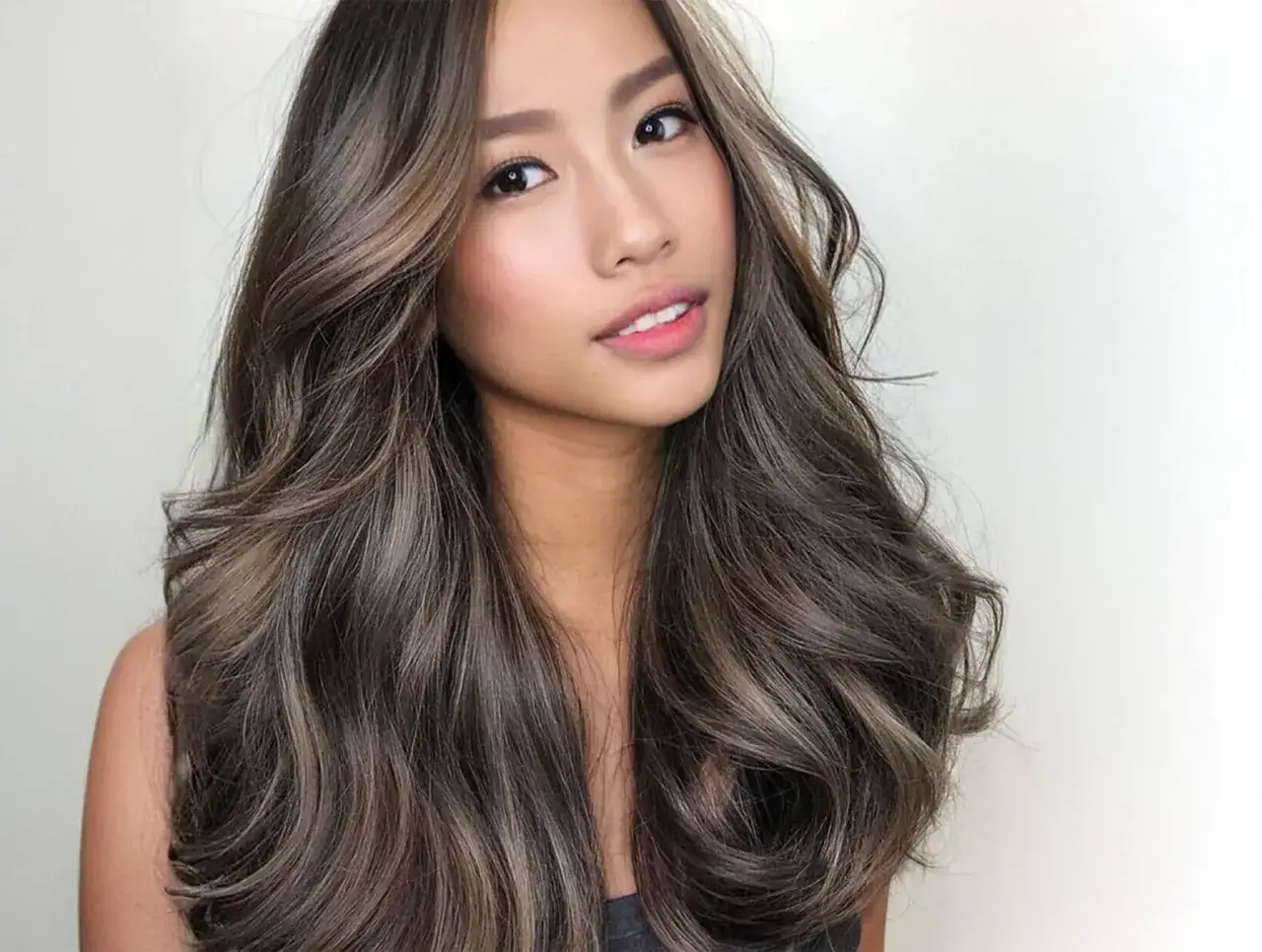 Mujer con cabello largo y ondulado, con reflejos pelo que le dan dimensión y brillo.