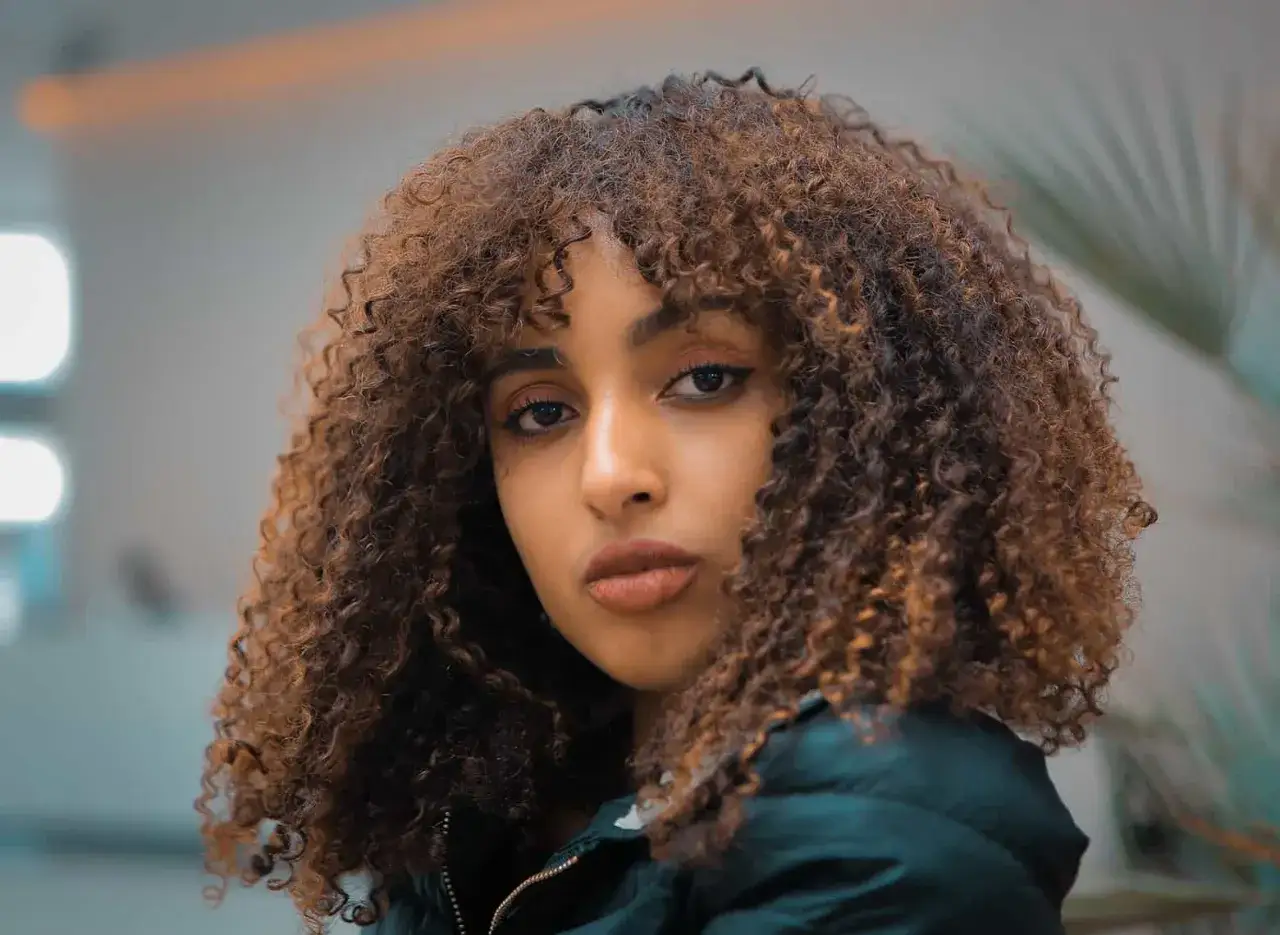 Mujer joven con recogido pelo rizado informal, con tonos castaños y cobrizos, mirada intensa.