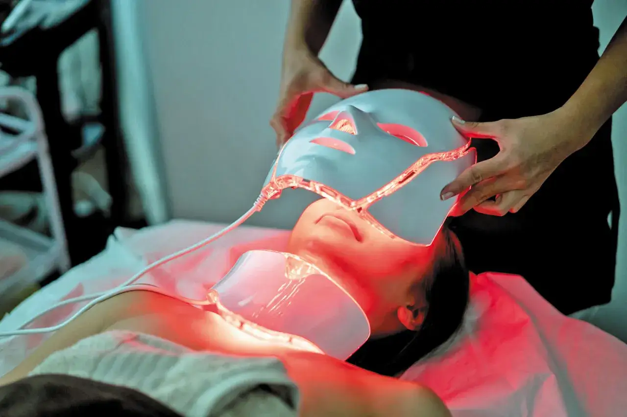 Una persona recibe tratamiento facial con máscara de luz roja, disfrutando de sus beneficios rejuvenecedores.