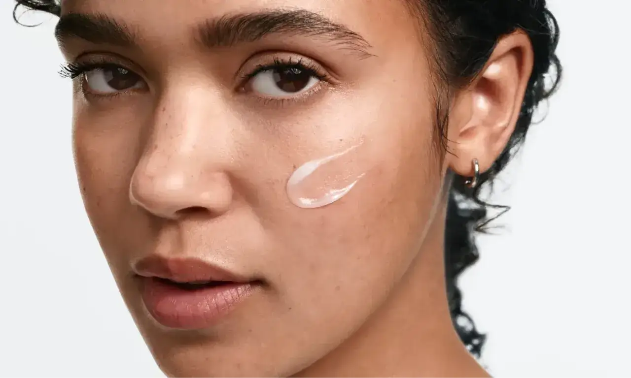 Una gota de crema deripil sobre la mejilla de una mujer, realzando su piel radiante.