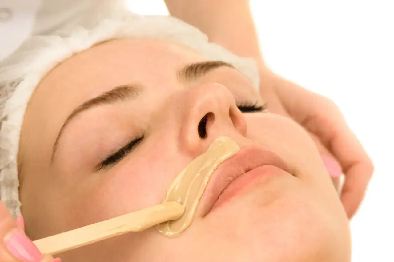 Aplicación de cera para depilación del bigote. Una espátula de madera extiende la cera tibia sobre el labio superior de una mujer.