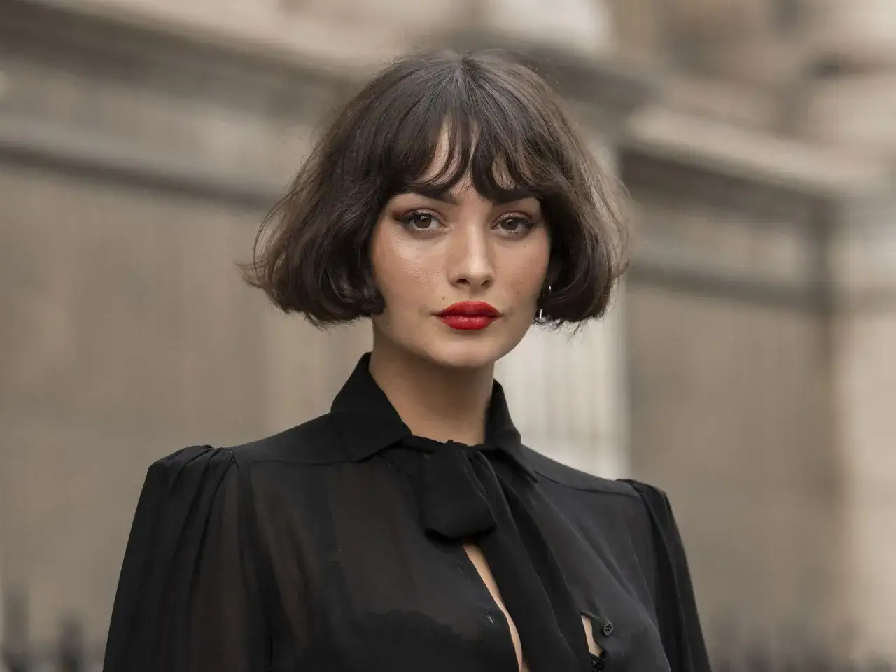 Mujer con un elegante corte de pelo french bob, labios rojos y un top negro transparente.