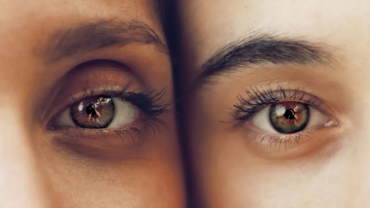 Dos ojos de cerca, uno con ojeras hundidas y el otro con piel lisa. Reflejo de un fotógrafo en ambos ojos.