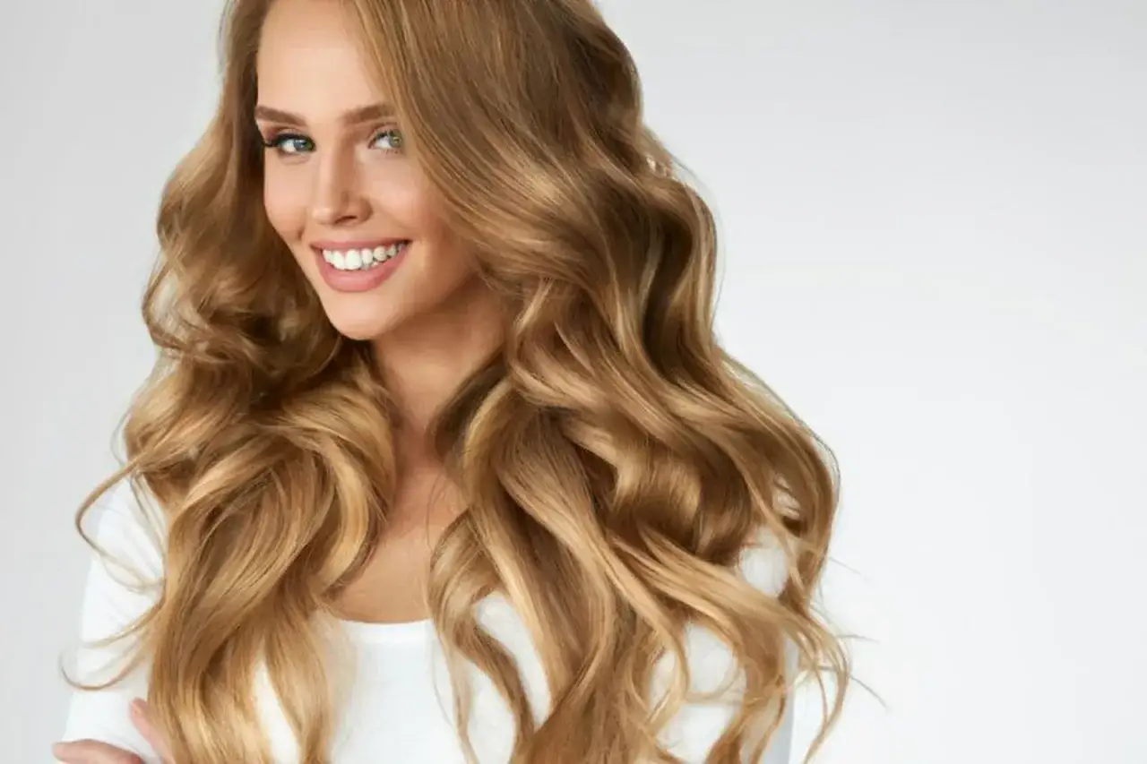 Mujer sonriente con cabello ondulado color miel rubio, que cae sobre sus hombros.