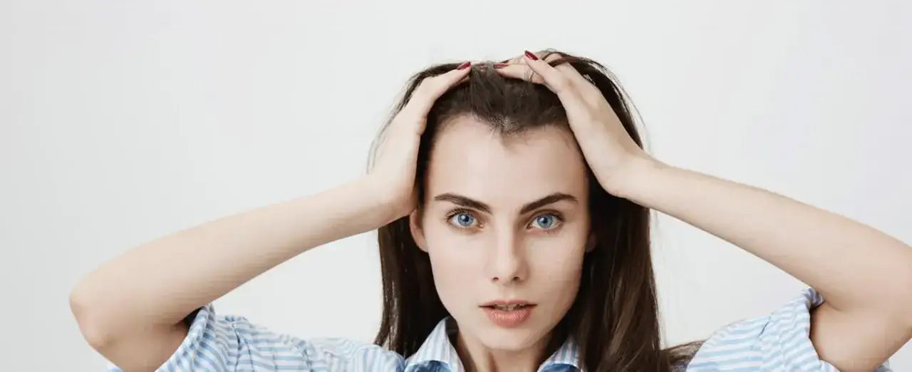 Mujer con cabello oscuro y ojos azules, se toca la frente con las manos, mostrando sus baby hairs.