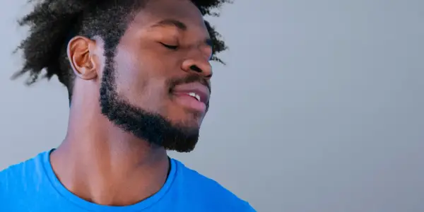 Hombre con ojos cerrados y barba cuidada, parece disfrutar de un momento de paz. Sus perillas resaltan su rostro.